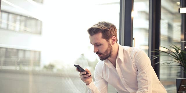 Man in a white button down shirt looks at his phone