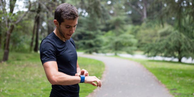 Man taking a break from running on a trail to check his smartwatch.