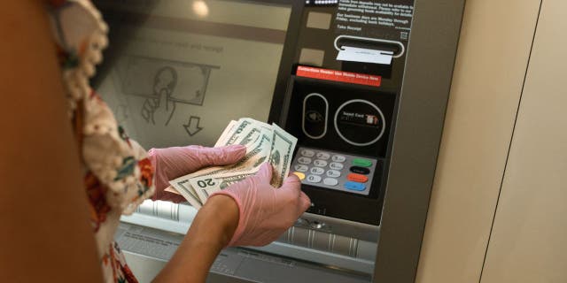 Wanita memegang uang tunai di depan ATM