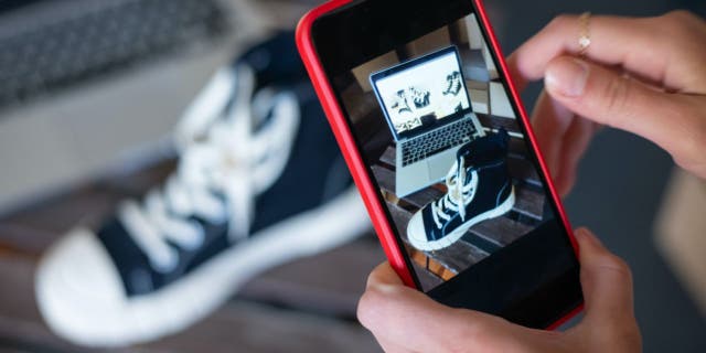 A person holding up a red phone taking a picture of a shoe.