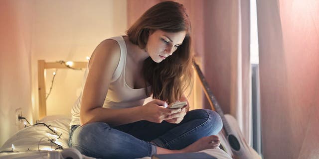 Woman sits in bedroom while texting on her phone