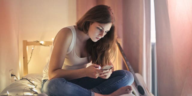 Woman sits in bedroom while texting on her phone