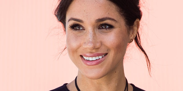 A close-up of Meghan Markle smiling wearing a black top and a black necklace