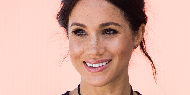 A close-up of Meghan Markle smiling wearing a black top and a black necklace