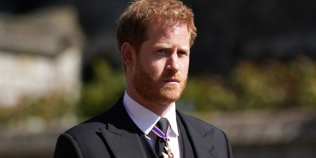 Prince Harry in a suit with medals looking sternly