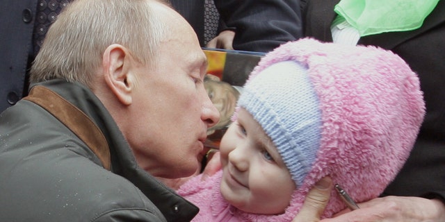 A file picture taken on May 29, 2010 shows former Russian Prime Minister, and now President Vladimir Putin kissing a baby during a visit to Nevskaya Dubrowka dormitory outside St. Petersburg. (Photo: ALEXEY DRUZHININ/AFP via Getty Images)