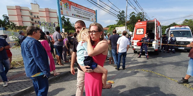A woman conforts a crying girl outside the day care center after a fatal attack on children in Blumenau, Brazil.