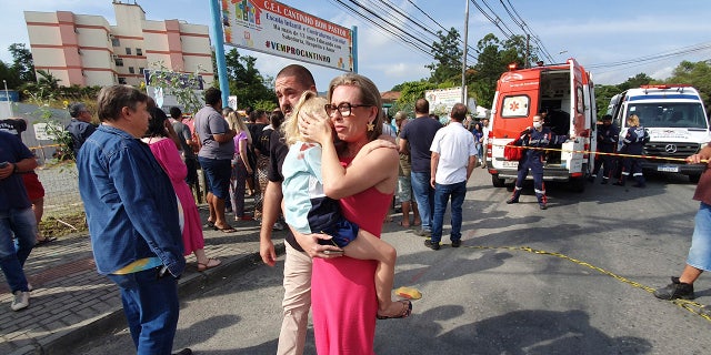 A woman conforts a crying girl outside the day care center after a fatal attack on children in Blumenau, Brazil.