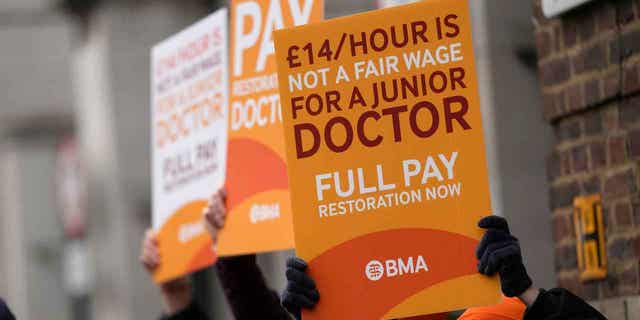 Médicos jóvenes sostienen carteles frente a un hospital en Londres, el 14 de marzo de 2023. Una huelga de cuatro días planeada por médicos en Inglaterra la próxima semana podría provocar el aplazamiento de un cuarto de millón de citas médicas.