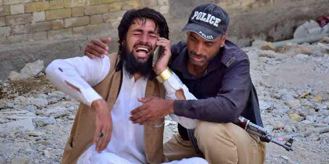 A police officer comforts a man mourning the death of a family member in the bomb blast, at a hospital, in Quetta, Pakistan, on April 10, 2023. A bomb targeting a police vehicle in Pakistan killed at least four people and wounded 15 others, on Monday.