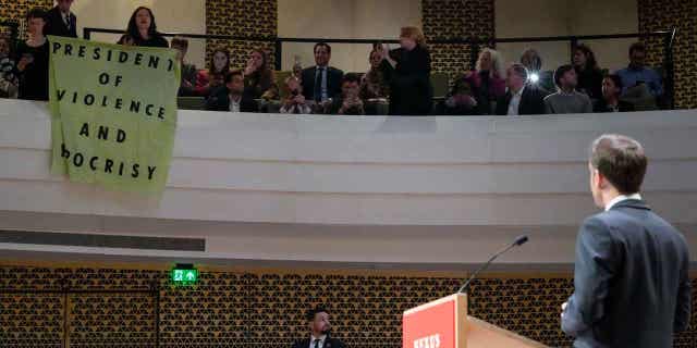 French President Emmanuel Macron looks at demonstrators unfolding a banner reading "President of Violence and Hypocrisy" during a speech in The Hague, Netherlands, on April 11, 2023.