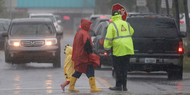 A school crossing guard helps people cross the street in the pouring rain at Dania Elementary School Wednesday, April 12, 2023 in Dania, Fla. 