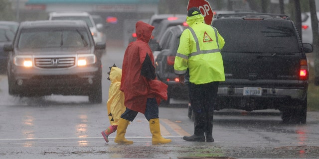 A school crossing guard helps people cross the street in the pouring rain at Dania Elementary School Wednesday, April 12, 2023 in Dania, Fla. 