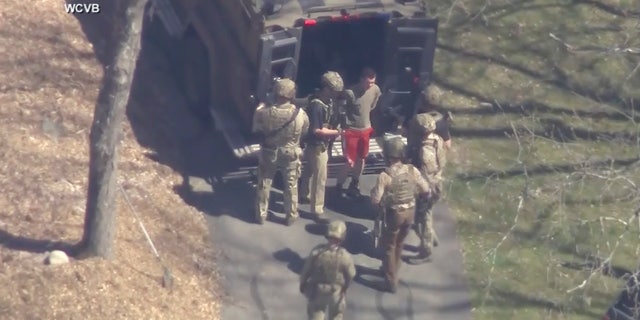 In this image made from video provided by WCVB-TV, Jack Teixeira, in T-shirt and shorts, is seen being taken into custody by armed tactical agents in Dighton, Massachusetts, on Thursday.