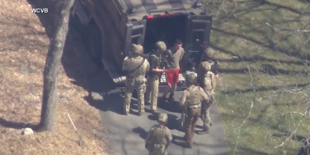 This image made from video provided by WCVB-TV, shows Jack Teixeira, in T-shirt and shorts, being taken into custody by armed tactical agents on Thursday, April 13, 2023, in Dighton, Massachusetts.