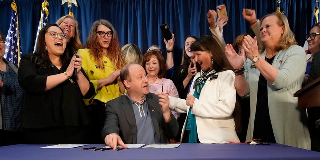 Colorado Gov. Jared Polis, front center, is applauded after he signed the first of three bills that enshrined protections for abortion and gender transition procedures and medications during a ceremony with bill sponsors and supporters in the State Capitol in Denver. 