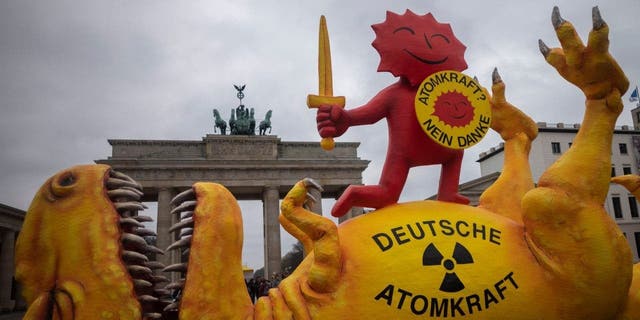Maketa dinosaura leži ispred Brandenburških vrata tijekom skupa kojim se obilježava zatvaranje nuklearne elektrane u Njemačkoj u Berlinu, Njemačka, subota, 15. travnja 2023.