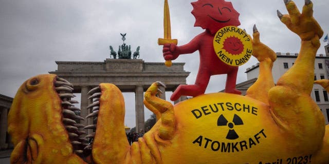 A mock-up dinosaur lies in front of the Brandenburg Gate during a rally marking the nuclear shutdown in Germany in Berlin, Germany, Saturday, April 15, 2023.