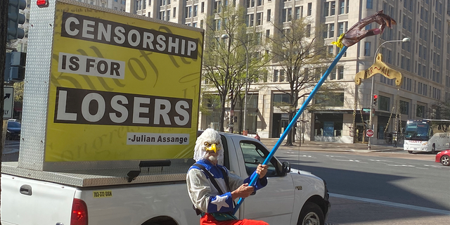 A man in an eagle costume is holding a "peace for all" sign at rally at the Justice Department opposing the prosecution of Julian Assange.