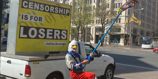 A man in an eagle costume is holding a "peace for all" sign at rally at the Justice Department opposing the prosecution of Julian Assange.