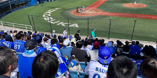 Aficionados con camisetas con el nombre y el número del beisbolista Trevor Bauer miran su lanzamiento en un estadio en Yokosuka, Japón, el domingo 16 de abril de 2023. Bauer lanzó cuatro entradas el domingo para el equipo de ligas menores Yokohama BayStars en Yokosuka mientras se preparan para dar inicio a su primer partido para el equipo de Yokohama.