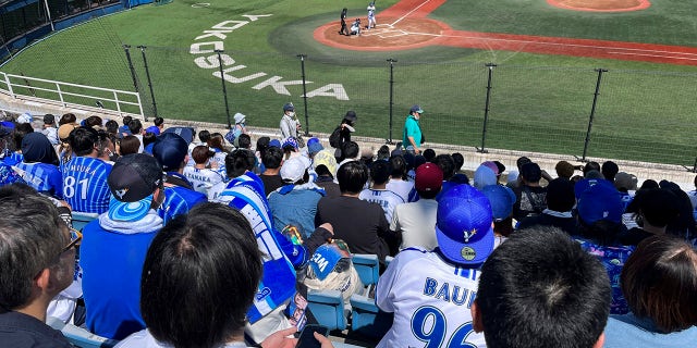 Aficionados con camisetas con el nombre y el número del beisbolista Trevor Bauer miran su lanzamiento en un estadio en Yokosuka, Japón, el domingo 16 de abril de 2023. Bauer lanzó cuatro entradas el domingo para el equipo de ligas menores Yokohama BayStars en Yokosuka mientras se preparan para dar inicio a su primer partido para el equipo de Yokohama.