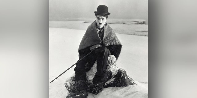 Charlie Chaplin sits wrapped in a blanket in the snow as The Lone Prospector in his 1925 film, "The Gold Rush."