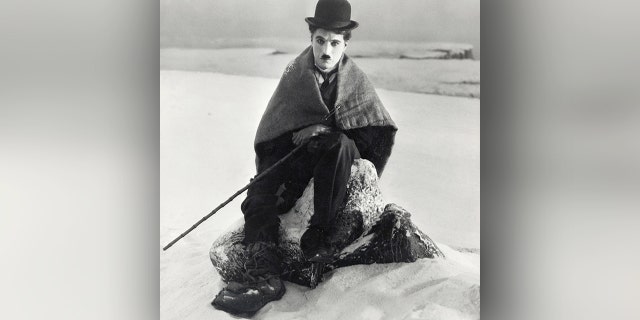 Charlie Chaplin sits wrapped in a blanket in the snow as The Lone Prospector in his 1925 film, "The Gold Rush."