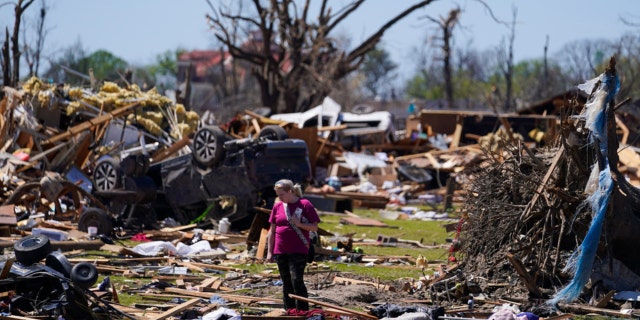 A woman walks near an uprooted tree, a flipped vehicle and debris from homes damaged by a tornado on March 27, 2023, in Rolling Fork, Miss.