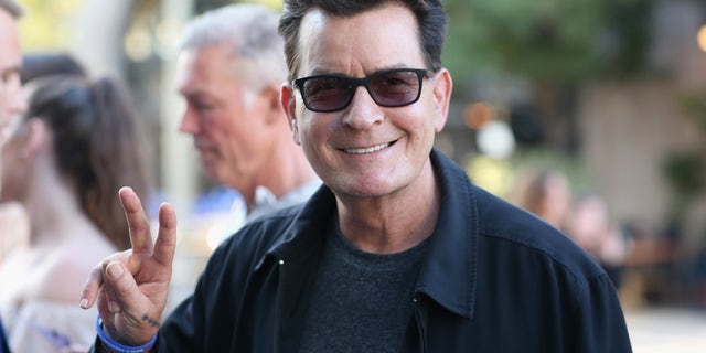 Charlie Sheen flashes a peace sign while wearing sunglasses.