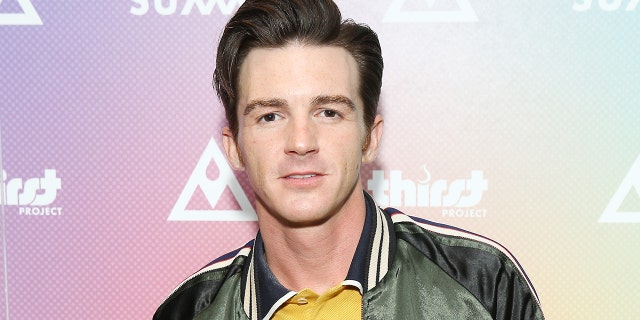 Drake Bell wears a green jacket and yellow under shirt with a blue striped collar on the red carpet