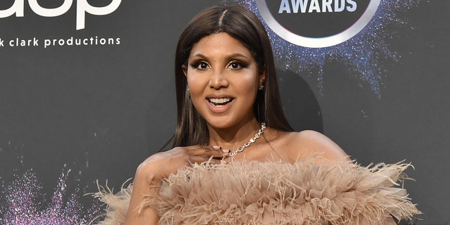 Toni Braxton smiles on the red carpet in a fluffy off-the-shoulder dark beige dress at the American Music Awards