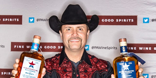 Singer-songwriter John Rich poses with bottles of Redneck Riviera Whiskey and Redneck Riviera Granny Rich Reserve Whiskey during the 2020 PHS Philadelphia Flower Show.