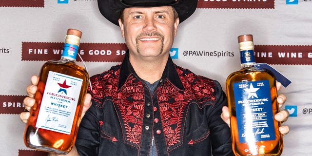 Singer-songwriter John Rich poses with bottles of Redneck Riviera Whiskey and Redneck Riviera Granny Rich Reserve Whiskey during the 2020 PHS Philadelphia Flower Show.