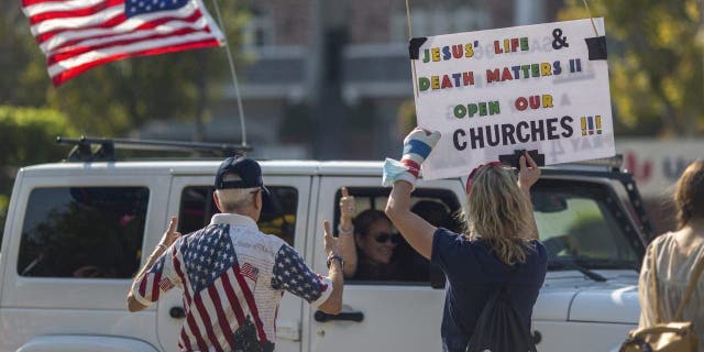 A woman holds a sign calling to "open our churches"