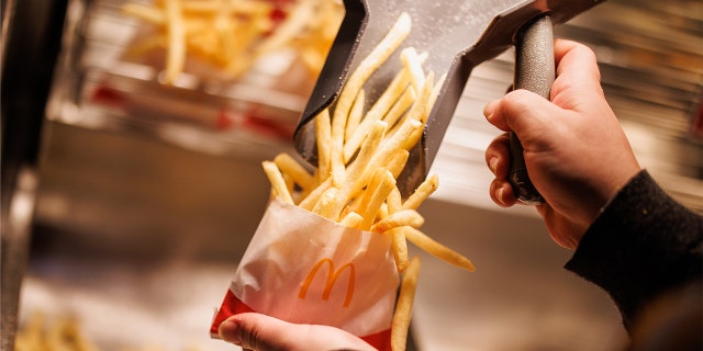 McDonald's kitchen employee shovels fries in small paper bag.