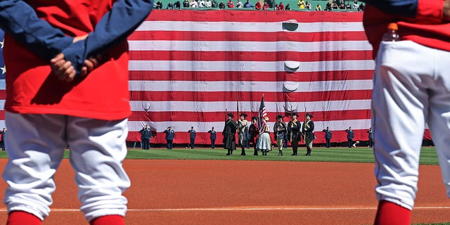 The giant American flag was unfurled over the Green Monster during the national anthem. The Boston Red Sox hosted the Minnesota Twins in the annual Patriots' Day morning MLB baseball game at Fenway Park in Boston on April 18, 2022. 