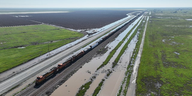 Allensworth, CA, Saturday, March 18, 2023 - A freight train travels past flooded land along Hwy 43, just north of Allensworth where residents are not waiting for government agencies to fortify a vulnerable levy in an effort to prevent floodwaters from inundating their community. (Robert Gauthier/Los Angeles Times via Getty Images)