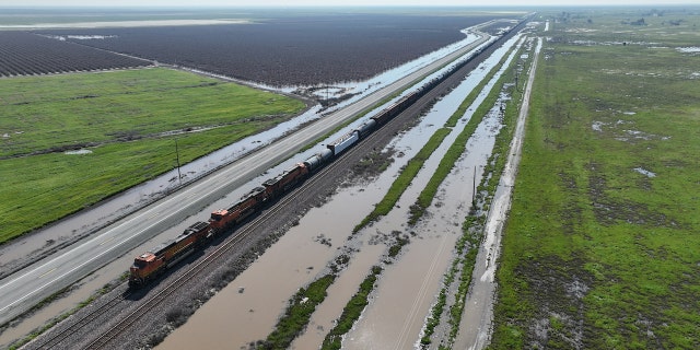 Allensworth, CA, Saturday, March 18, 2023 - A freight train travels past flooded land along Hwy 43, just north of Allensworth where residents are not waiting for government agencies to fortify a vulnerable levy in an effort to prevent floodwaters from inundating their community. (Robert Gauthier/Los Angeles Times via Getty Images)