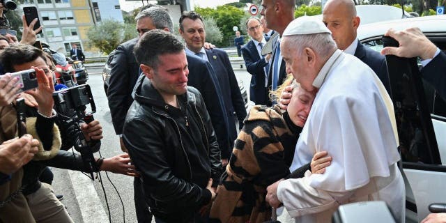 Pope Francis embraces Serena Subania as her husband Matteo Rugghia (L), a couple who lost their five-year-old son the day before, reacts as the Pope leaves the Gemelli Polyclinic April 1, 2023 in Rome, after being discharged after his cures for bronchitis.