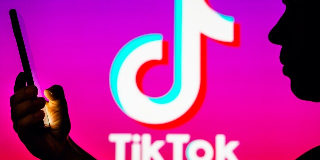 In this photo illustration, a woman's silhouette holds a smartphone with the TikTok logo in the background.