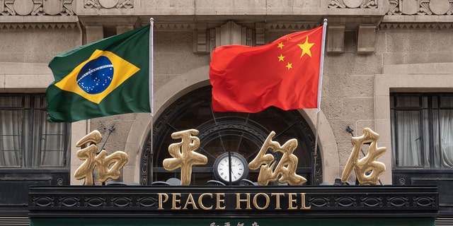 Chinese and Brazilian national flags flutter in the wind above the main entrance of the Peace Hotel on Nanjing Road Pedestrian street in Shanghai, China, April 13, 2023. 