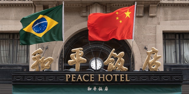 Chinese and Brazilian national flags flutter in the wind above the main entrance of the Peace Hotel on Nanjing Road Pedestrian street in Shanghai, China, April 13, 2023. 