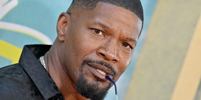 Jamie Foxx bites on his sunglasses ear piece while posing in front of the camera on the red carpet