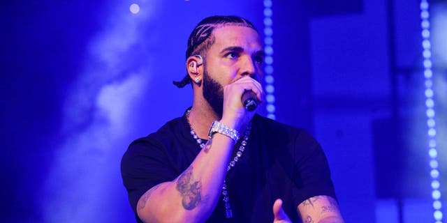 Drake in a short sleeve black shirt performs on stage rapping into a microphone