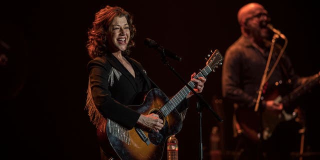 amy grant smiling while playing guitar on stage during tour