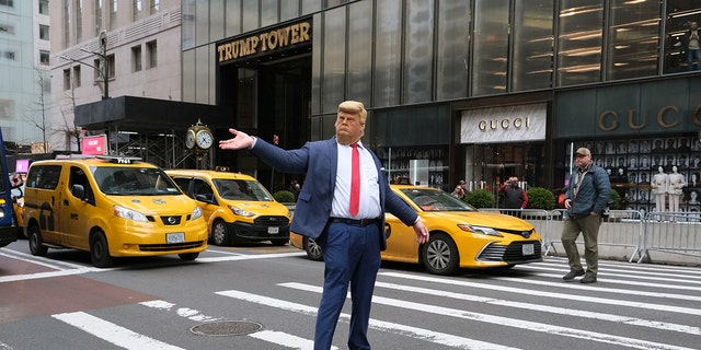 A person wears a mask depicting former president Donald Trump and poses outside of Trump Tower on March 31, 2023, in New York City. Trump has been indicted for his role in a hush-money scheme before the 2016 election. 