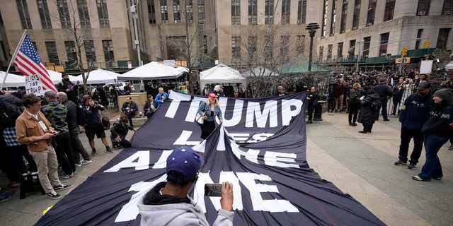 A supporter of former President Donald Trump stands on a banner criticizing him outside the courthouse where Trump will arrive later in the day for his arraignment.
