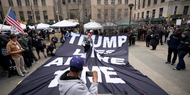 A supporter of former President Donald Trump stands on a banner criticizing him outside the courthouse where Trump will arrive later in the day for his arraignment.