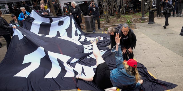 The Trump supporter is confronted by anti-Trump protesters while laying on the ground.